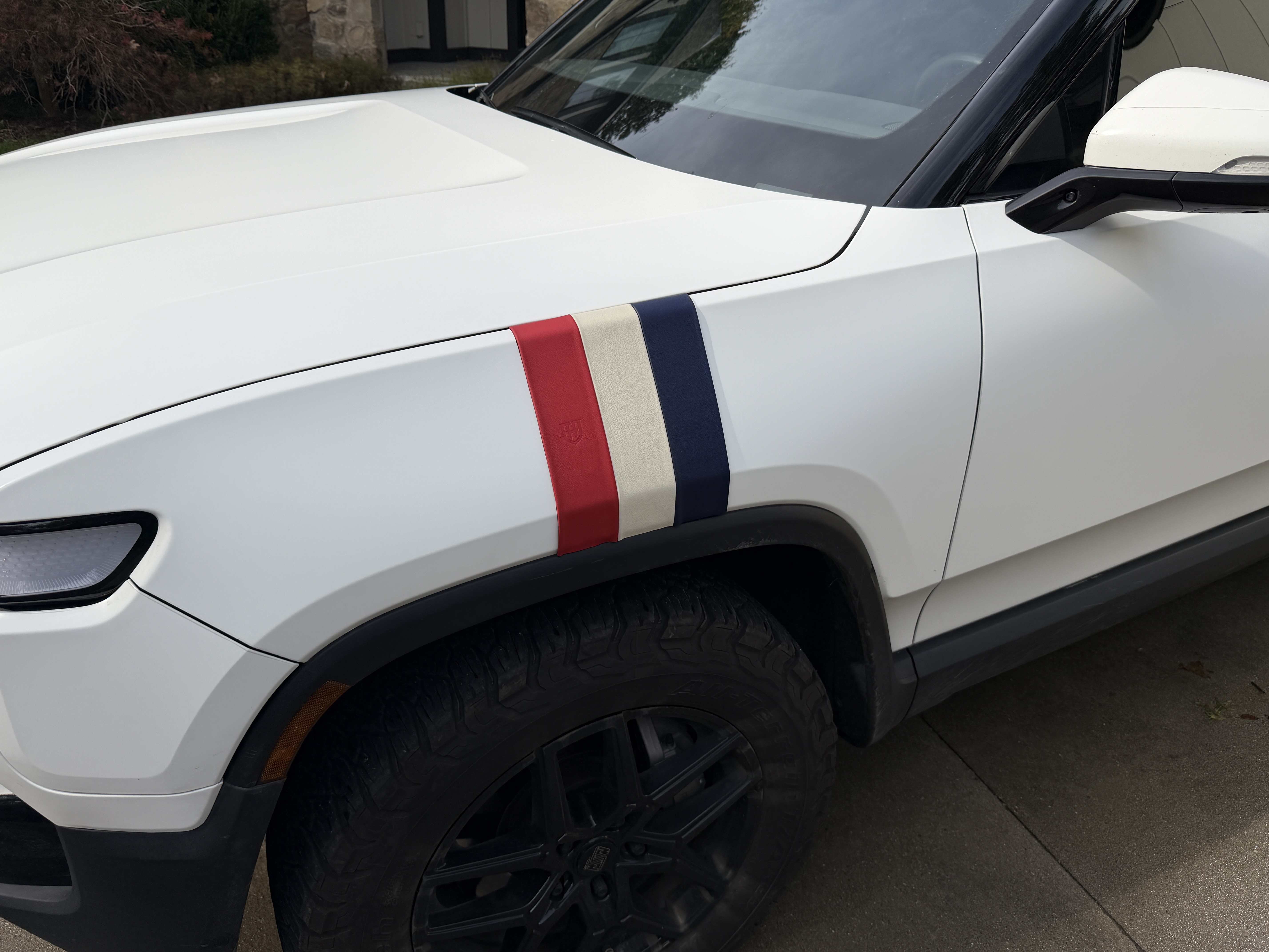 Red, cream and navy leather stripes arranged together across the front fender of a white Rivian