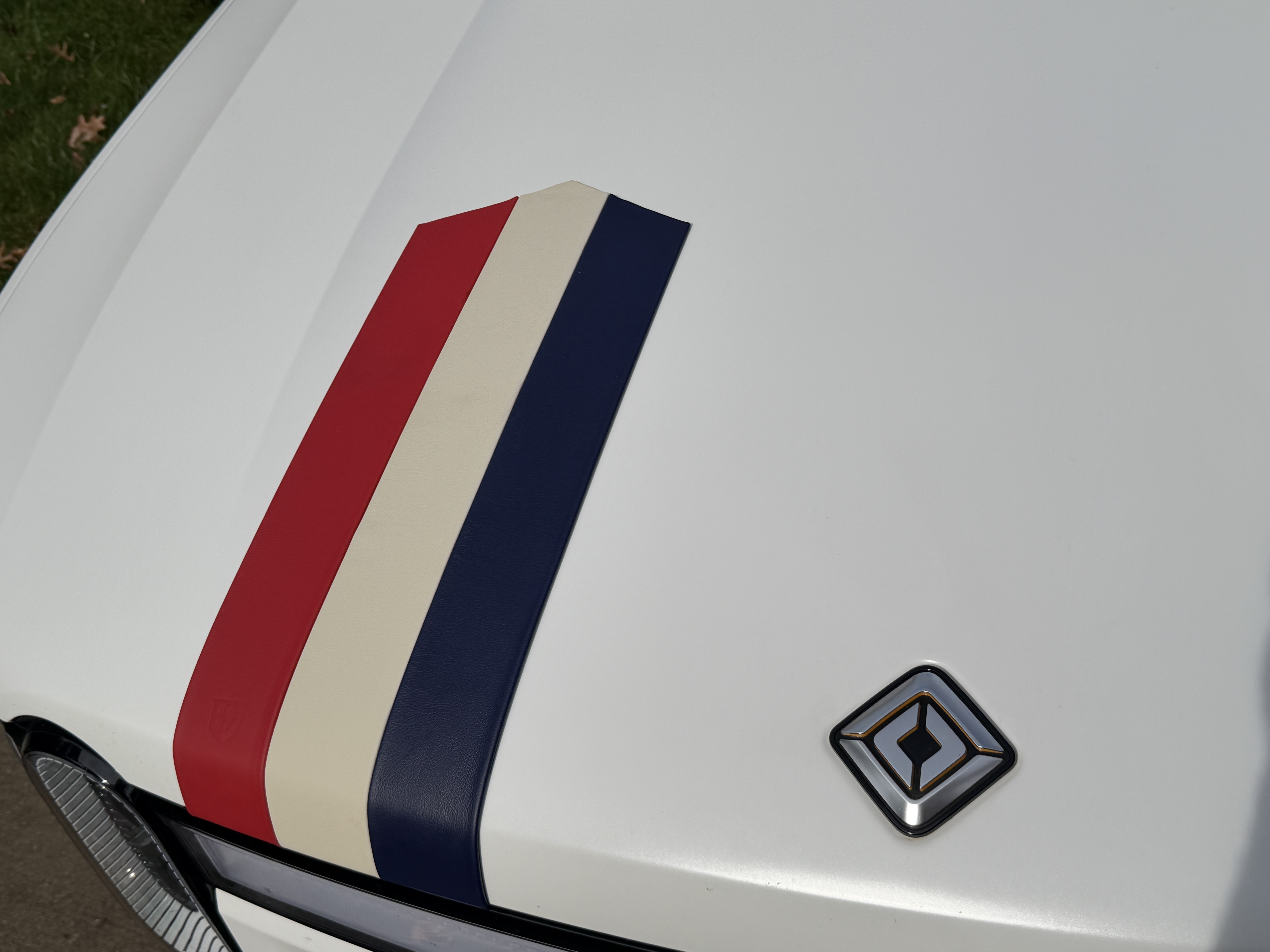 The same red, cream and navy leather stripes rearranged lengthwise on the hood of the white Rivian